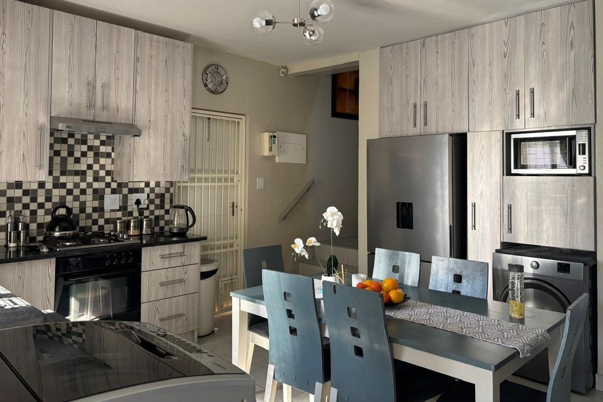 Open-plan kitchen and dining area featuring wood-grain cabinetry, a gas hob, extractor fan, and integrated appliances, leading to a staircase.