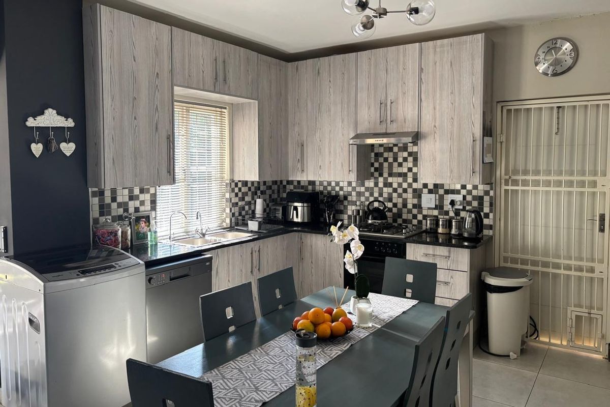 Open-plan kitchen featuring wood-look cabinetry, granite-style countertops, a gas hob, and a tiled backsplash, seamlessly integrated with a dining area.