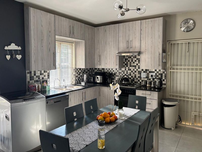 Open-plan kitchen featuring wood-look cabinetry, granite-style countertops, a gas hob, and a tiled backsplash, seamlessly integrated with a dining area.