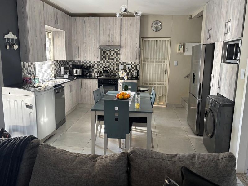 Open-plan kitchen featuring wood-look cabinetry, tiled flooring, and integrated appliances, seamlessly connecting to the dining area.