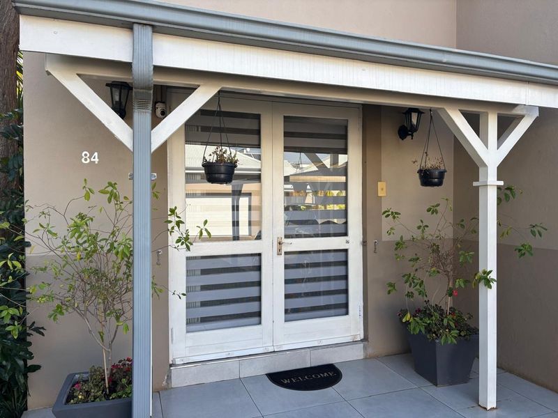 The front entrance features a covered porch with tiled flooring, double glass doors, and wall-mounted exterior lighting.