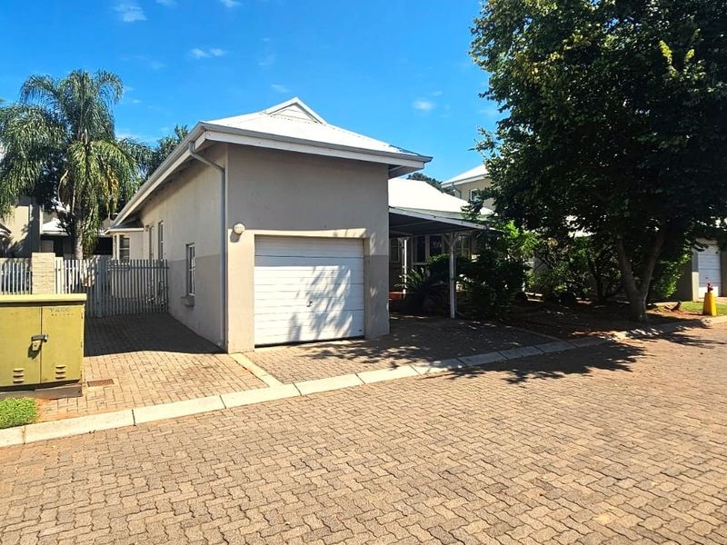 Exterior view of a townhouse complex featuring a paved driveway, single garage, and well-maintained surrounding grounds.