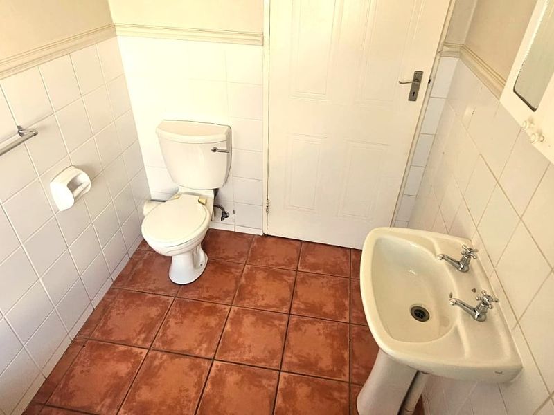 A functional guest bathroom featuring a pedestal basin, toilet, and tiled finishes, offering a clean space ready for modern updates.