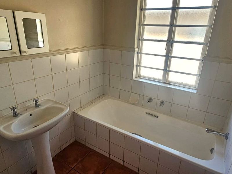 A dated bathroom featuring a pedestal basin, built-in bathtub, and tiled finishes, offering a blank canvas for modern renovation and updates.