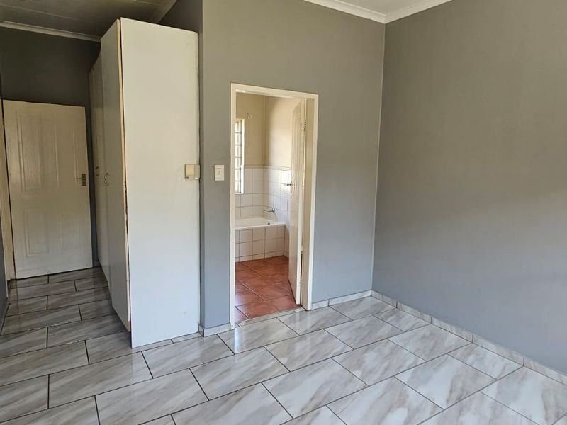 A vacant bedroom featuring neutral grey walls, modern marble-look tiled flooring, and built-in cupboards, with direct access to an en-suite bathroom.