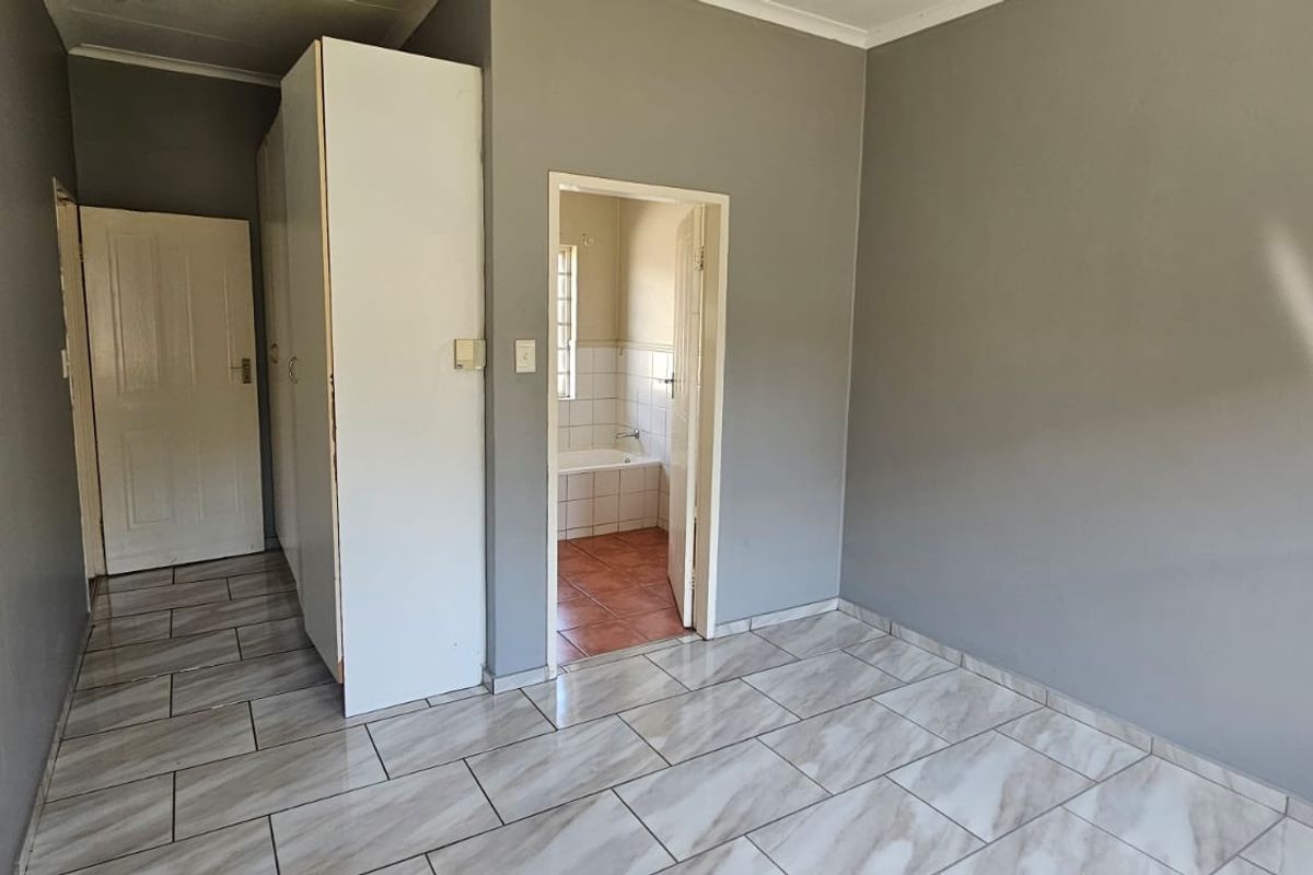 A vacant bedroom featuring neutral grey walls, modern marble-look tiled flooring, and built-in cupboards, with direct access to an en-suite bathroom.
