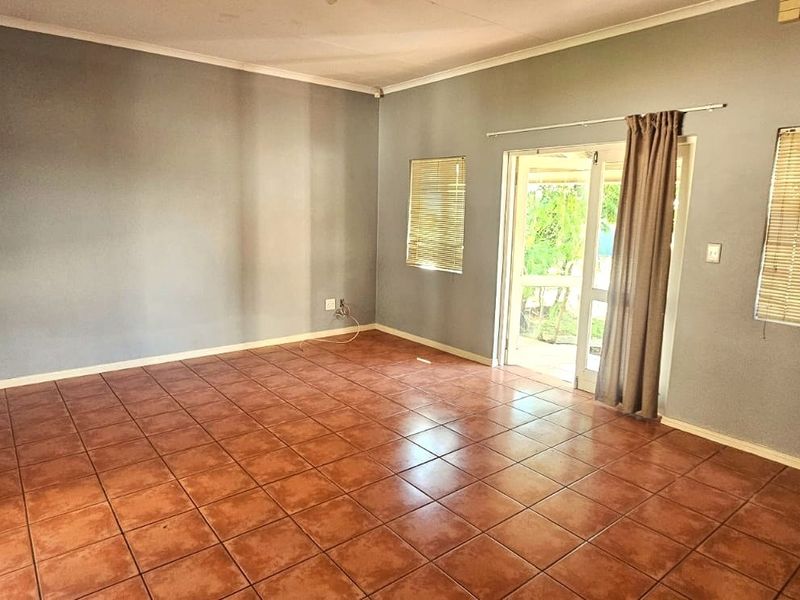 An empty living room featuring ceramic tile flooring, neutral grey walls, and a sliding glass door providing access to the outdoor area.