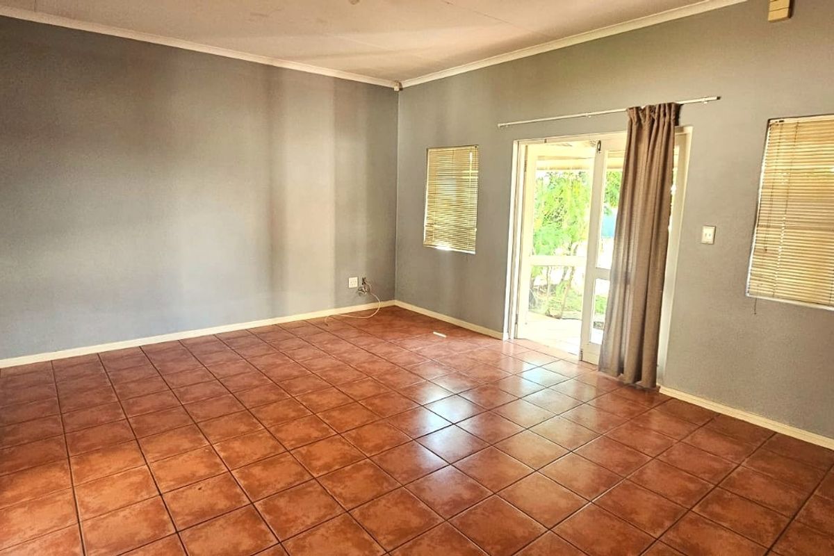 An empty living room featuring ceramic tile flooring, neutral grey walls, and a sliding glass door providing access to the outdoor area.