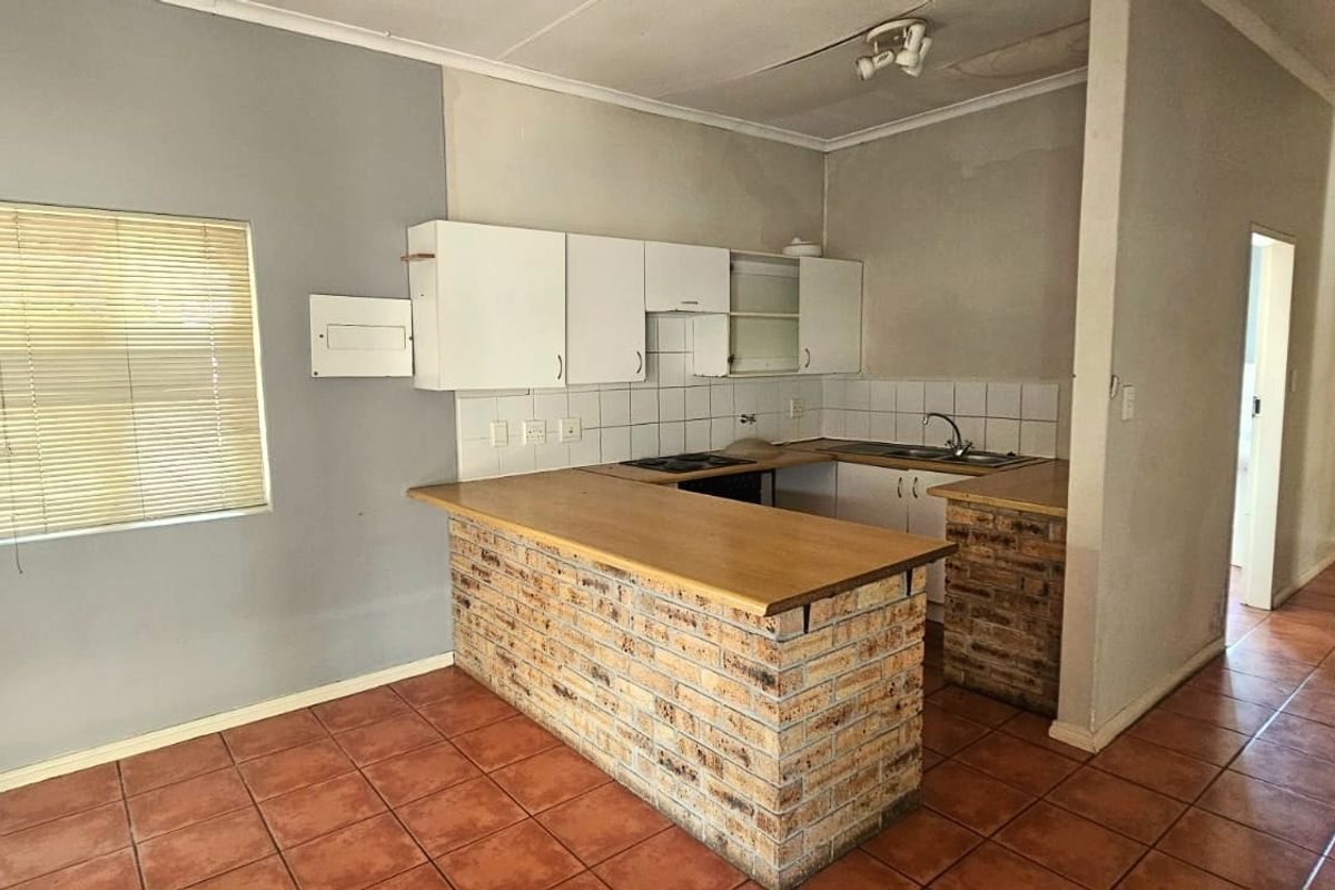 A dated kitchen featuring a brick-base breakfast bar, built-in cabinetry, and tiled flooring, offering significant potential for a modern renovation.