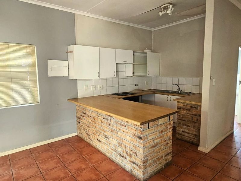 A dated kitchen featuring a brick-base breakfast bar, built-in cabinetry, and tiled flooring, offering significant potential for a modern renovation.