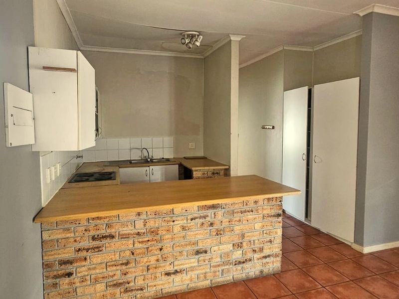 An open-plan kitchen featuring a brick breakfast bar, laminate countertops, built-in hob, and tiled flooring, offering a functional space ready for modernization.