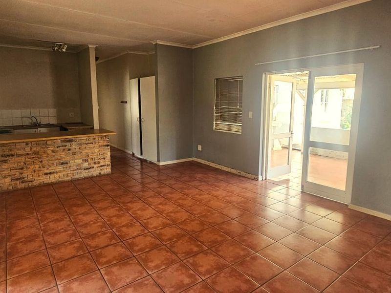 Open-plan living and kitchen area featuring ceramic tile flooring, a brick-faced breakfast bar, and direct access to an outdoor patio through sliding glass doors.