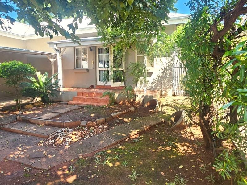 Front exterior view of the townhouse featuring a covered porch, paved walkway, and an attached carport area surrounded by established garden landscaping.
