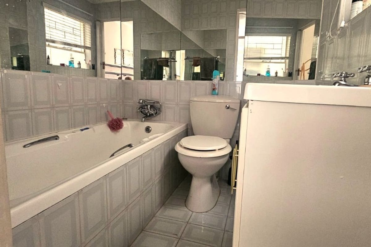 A functional bathroom featuring a bathtub, toilet, and vanity with wall-to-wall mirrors and dated tiled finishes.
