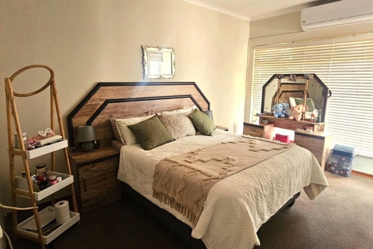 A bedroom featuring a built-in headboard, split-system air conditioning, and venetian blinds, providing a functional and comfortable living space.
