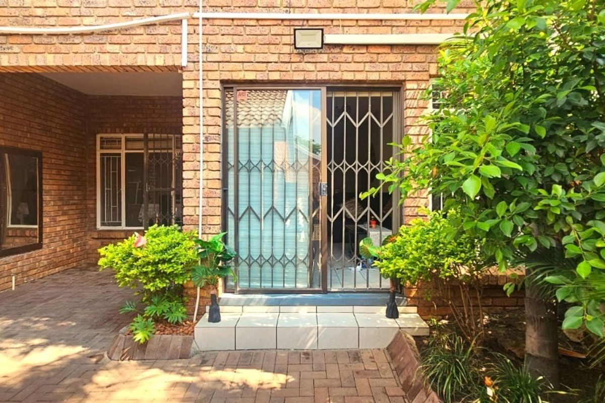 Rear exterior view of the townhouse featuring a brick facade, paved patio area, and a sliding glass door with a security gate.