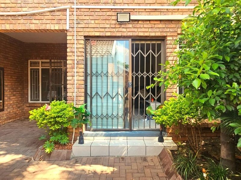 Rear exterior view of the townhouse featuring a brick facade, paved patio area, and a sliding glass door with a security gate.