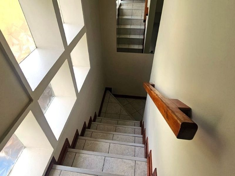 A staircase featuring tiled steps, a wooden handrail, and a grid-style window providing natural light to the hallway area.