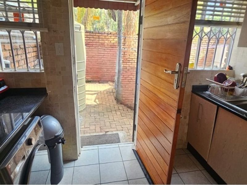 A functional scullery area featuring granite countertops, a stainless steel sink, and direct access to an outdoor courtyard space.