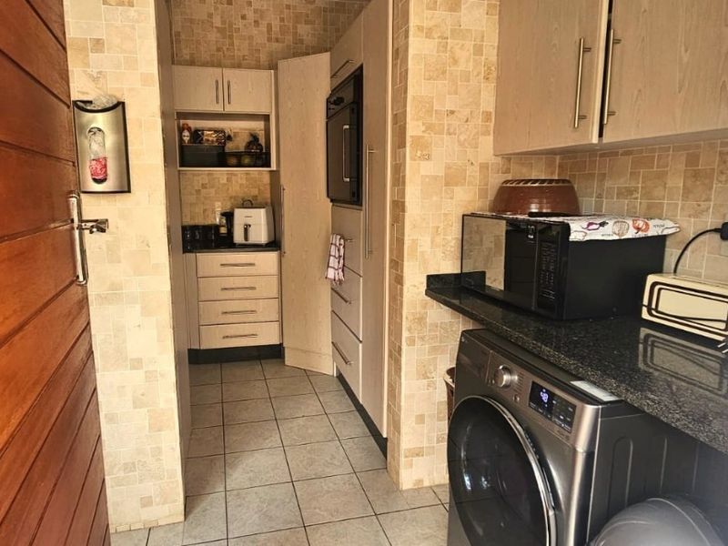 A functional scullery area featuring built-in cabinetry, granite countertops, tiled backsplash, and dedicated laundry plumbing connections.