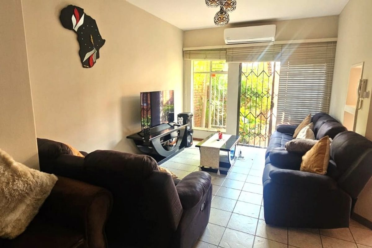 A comfortable living room featuring tiled flooring, a wall-mounted air conditioner, and a sliding glass door providing access to the outdoor area.