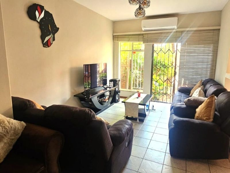 A comfortable living room featuring tiled flooring, a wall-mounted air conditioner, and a sliding glass door providing access to the outdoor area.