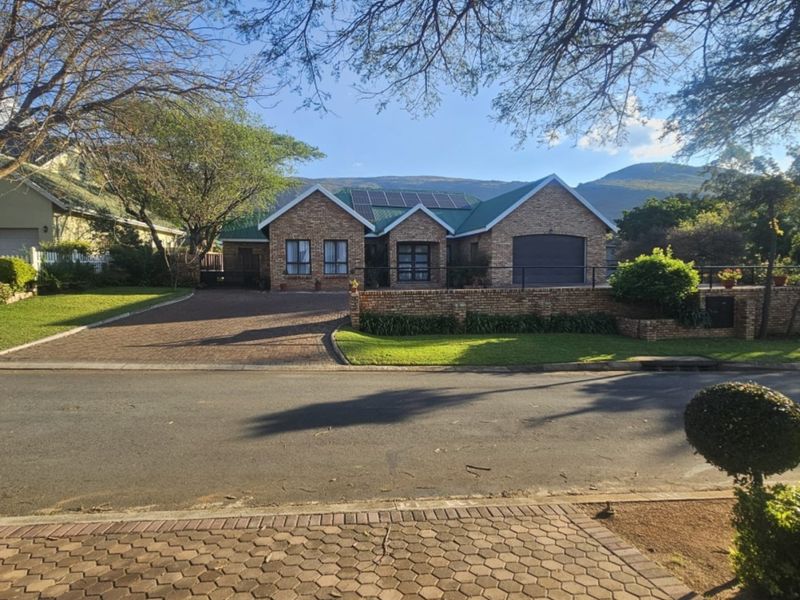 A well-maintained brick house featuring a paved driveway, integrated garage, and solar panels, set against a scenic mountain backdrop.