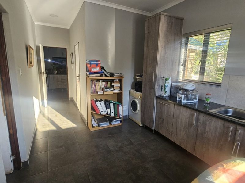 A functional scullery area featuring built-in cabinetry, granite countertops, a stainless steel sink, and dedicated plumbing for laundry appliances.