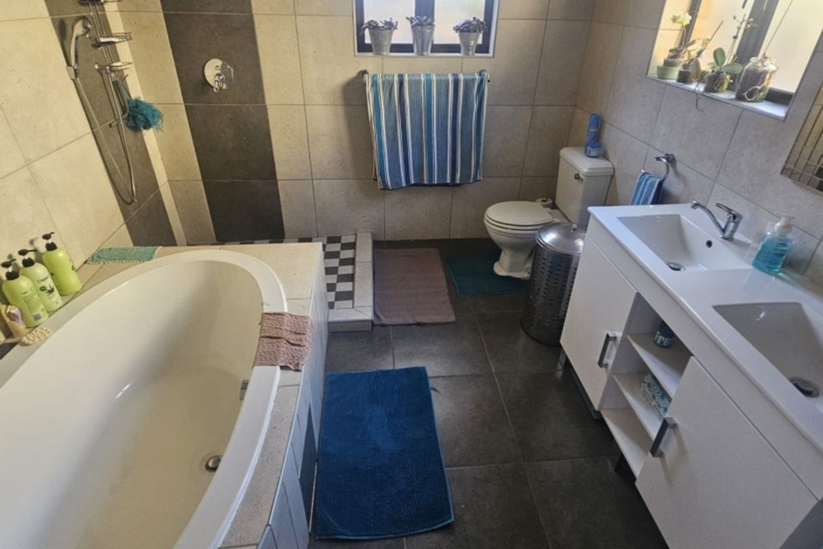 A well-appointed bathroom featuring a built-in bathtub, a modern double vanity, a toilet, and neutral-toned wall and floor tiling.