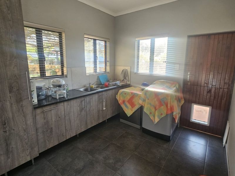 A functional laundry room featuring built-in wood-look cabinetry, granite countertops, a stainless steel sink, and tiled flooring with direct outdoor access.
