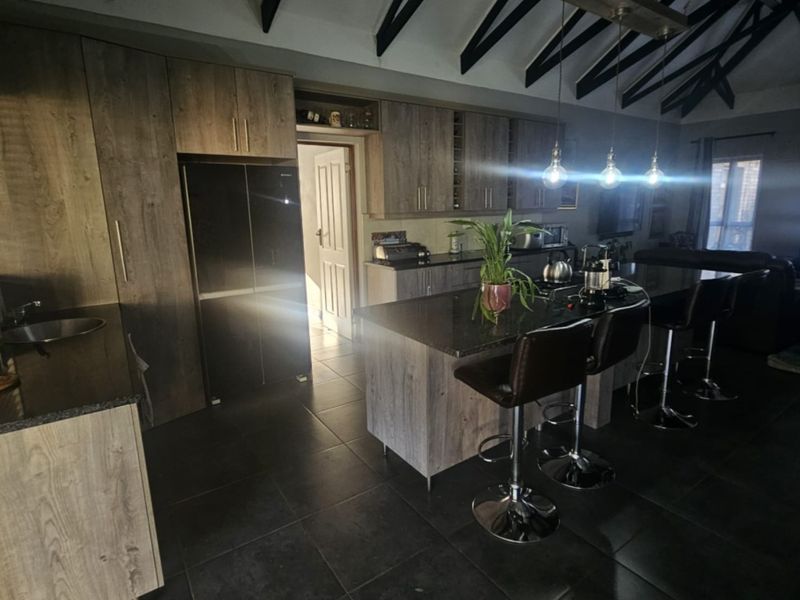 Spacious open-plan kitchen featuring modern wood-finish cabinetry, granite countertops, a central island, and striking exposed timber rafters under a high ceiling.