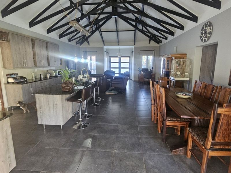 Spacious open-plan living area featuring high vaulted ceilings with exposed timber trusses, a modern kitchen with island, and large format floor tiles.
