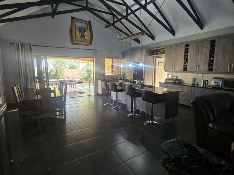 Spacious open-plan living and kitchen area featuring high vaulted ceilings with exposed trusses, modern cabinetry, and seamless flow to the outdoor patio.