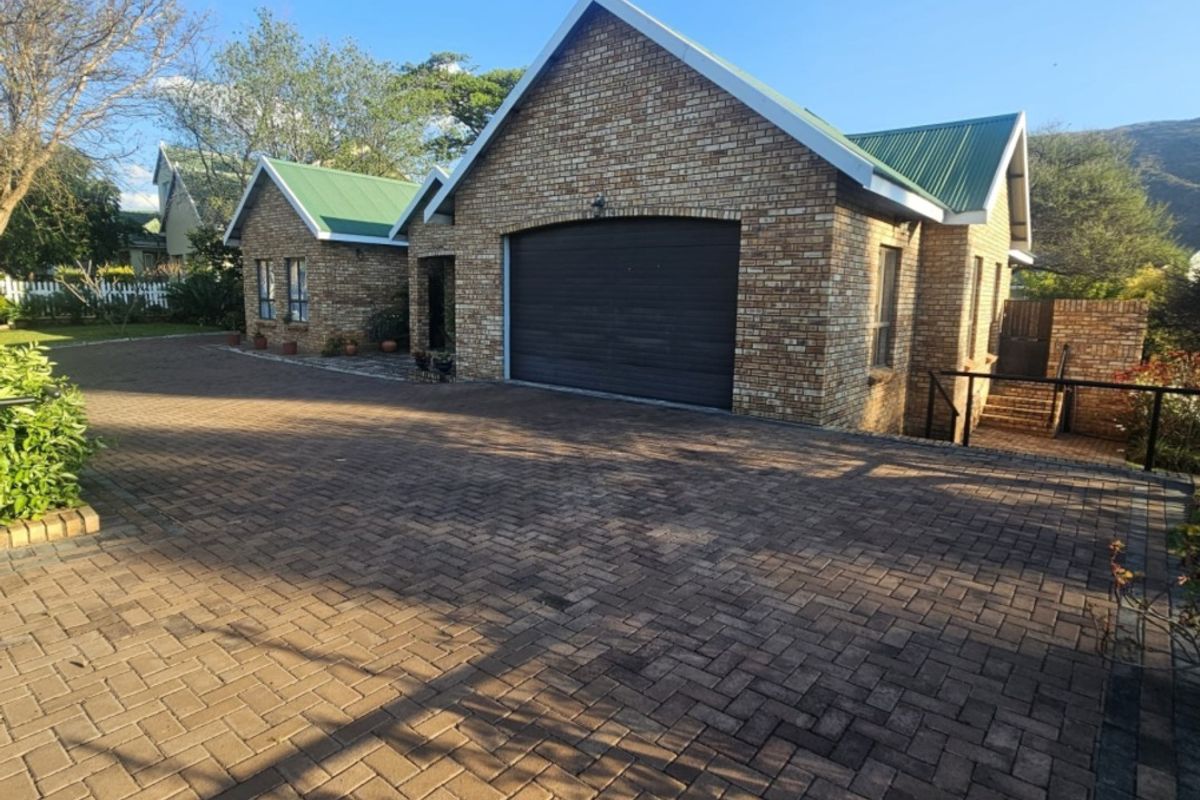 A well-maintained face brick house featuring a green metal roof, a paved driveway, and an integrated single garage.