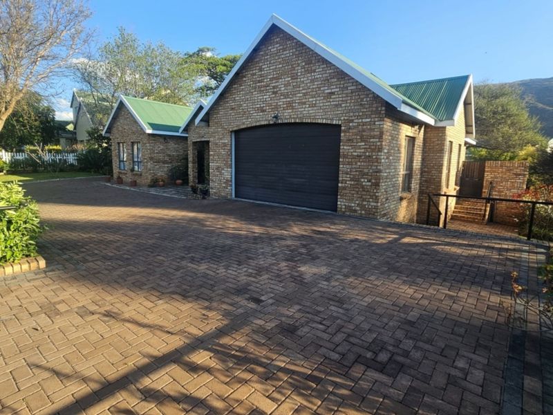 A well-maintained face brick house featuring a green metal roof, a paved driveway, and an integrated single garage.