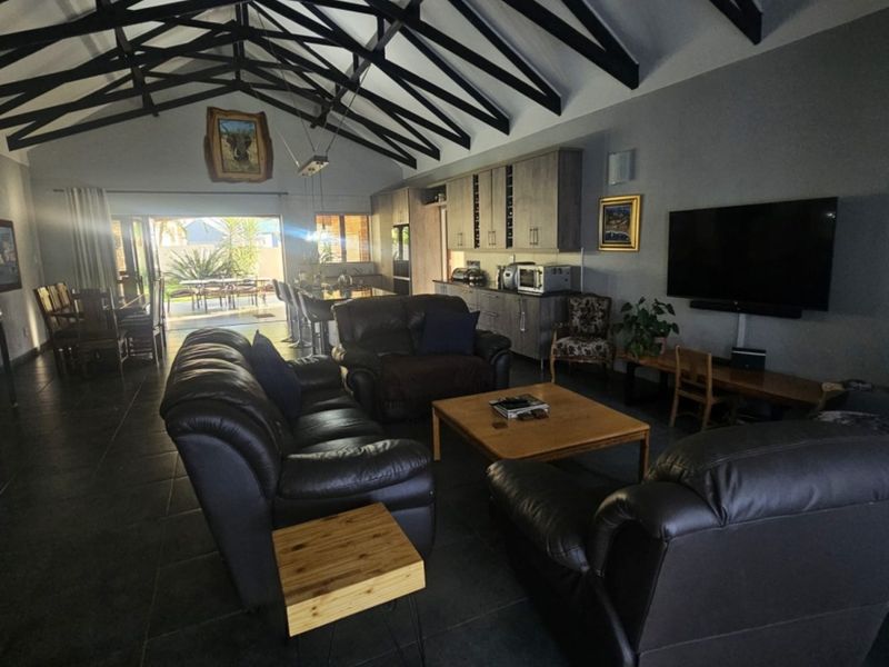 Spacious open-plan living area featuring high vaulted ceilings with exposed trusses, modern tiled flooring, and seamless flow to an outdoor patio.