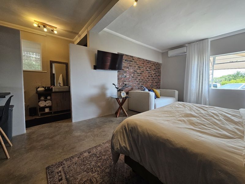 A modern bedroom featuring polished concrete floors, an exposed brick accent wall, and an integrated vanity area with contemporary finishes.