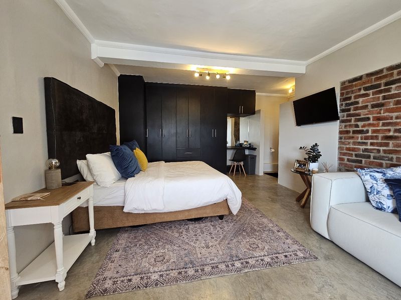 Spacious bedroom featuring polished concrete floors, extensive built-in cabinetry, and a rustic exposed brick feature wall.