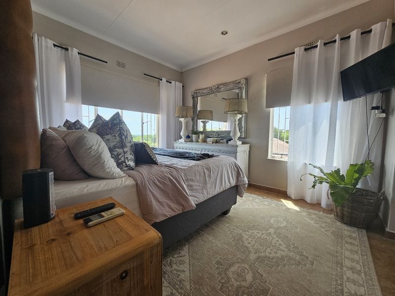 A well-lit bedroom featuring neutral wall tones, large windows with security bars, and recessed ceiling lighting, creating a comfortable and functional living space.