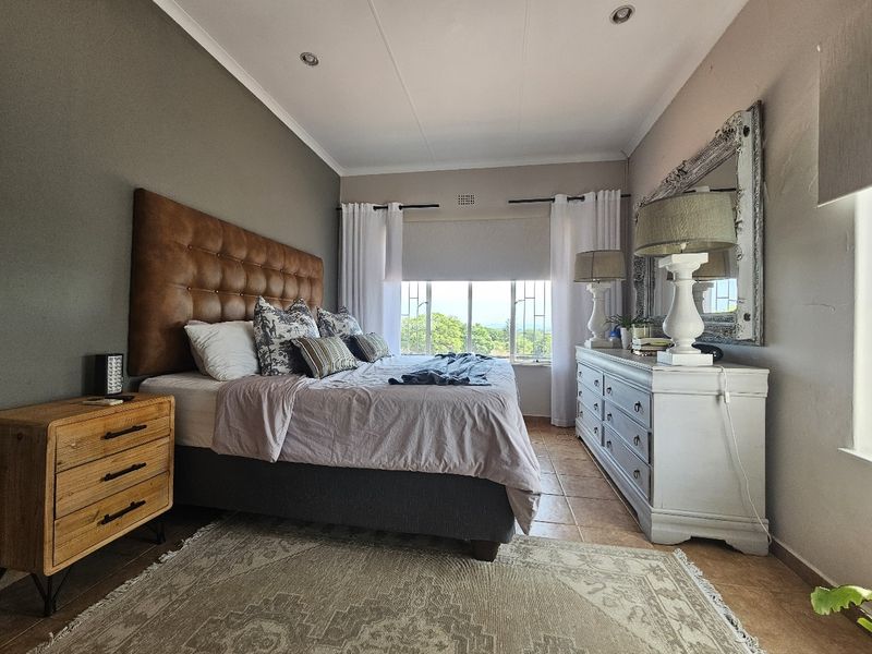 A well-maintained bedroom featuring tiled flooring, recessed downlighting, and a large window with security bars providing natural light and exterior views.
