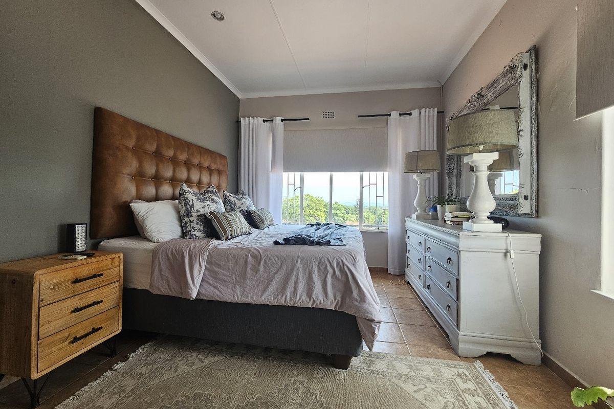 A well-maintained bedroom featuring tiled flooring, recessed downlighting, and a large window with security bars providing natural light and exterior views.