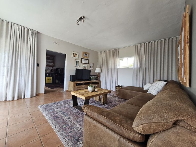 A comfortable living room featuring tiled flooring and large windows with floor-to-ceiling curtains, providing a bright and inviting space for relaxation.