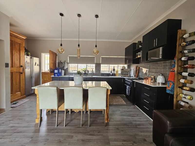 Modern kitchen featuring dark cabinetry, stone countertops, a central island with seating, and stylish pendant lighting.