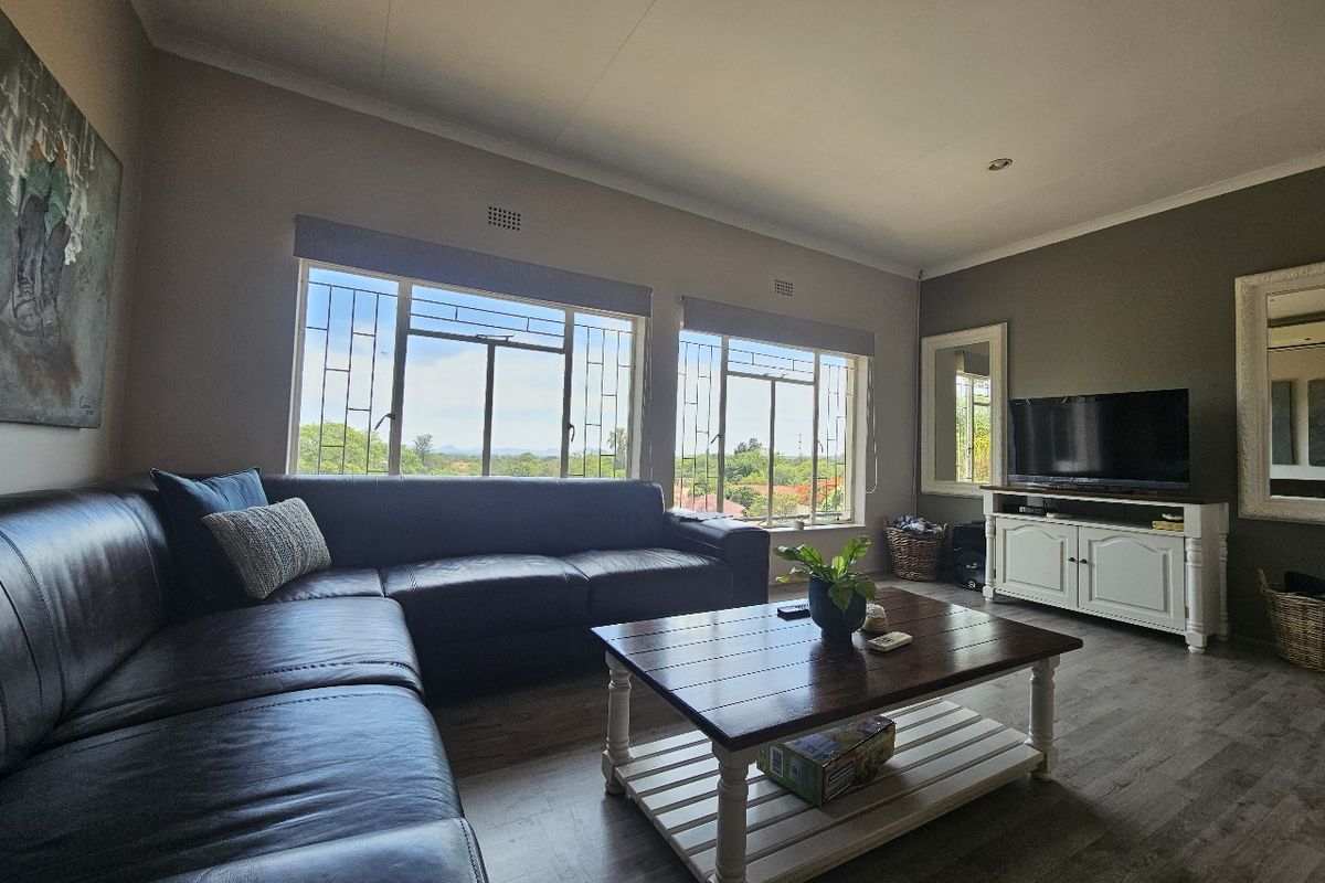 A comfortable living room featuring laminate flooring, large windows with security bars, and neutral wall tones, offering a bright and functional space.