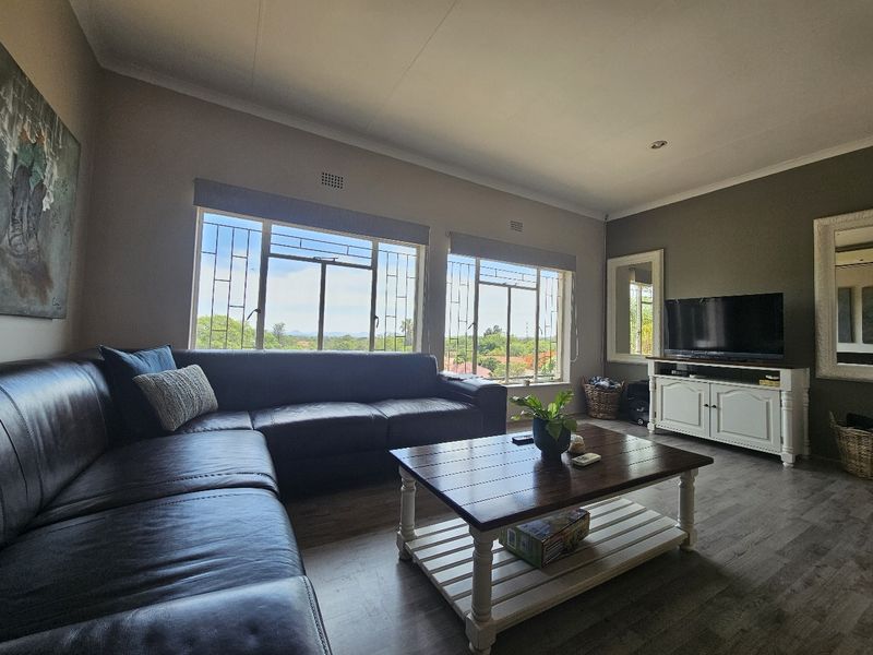 A comfortable living room featuring laminate flooring, large windows with security bars, and neutral wall tones, offering a bright and functional space.