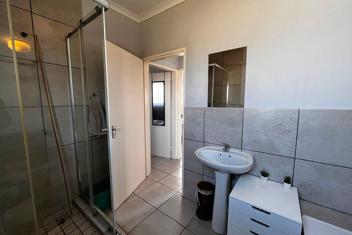 A functional bathroom featuring a glass shower enclosure, pedestal basin, and neutral wall and floor tiling.