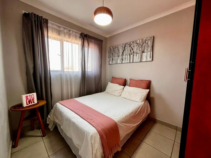 A cozy bedroom featuring neutral wall tones, tiled flooring, and a central pendant light fixture, providing a comfortable and functional sleeping space.