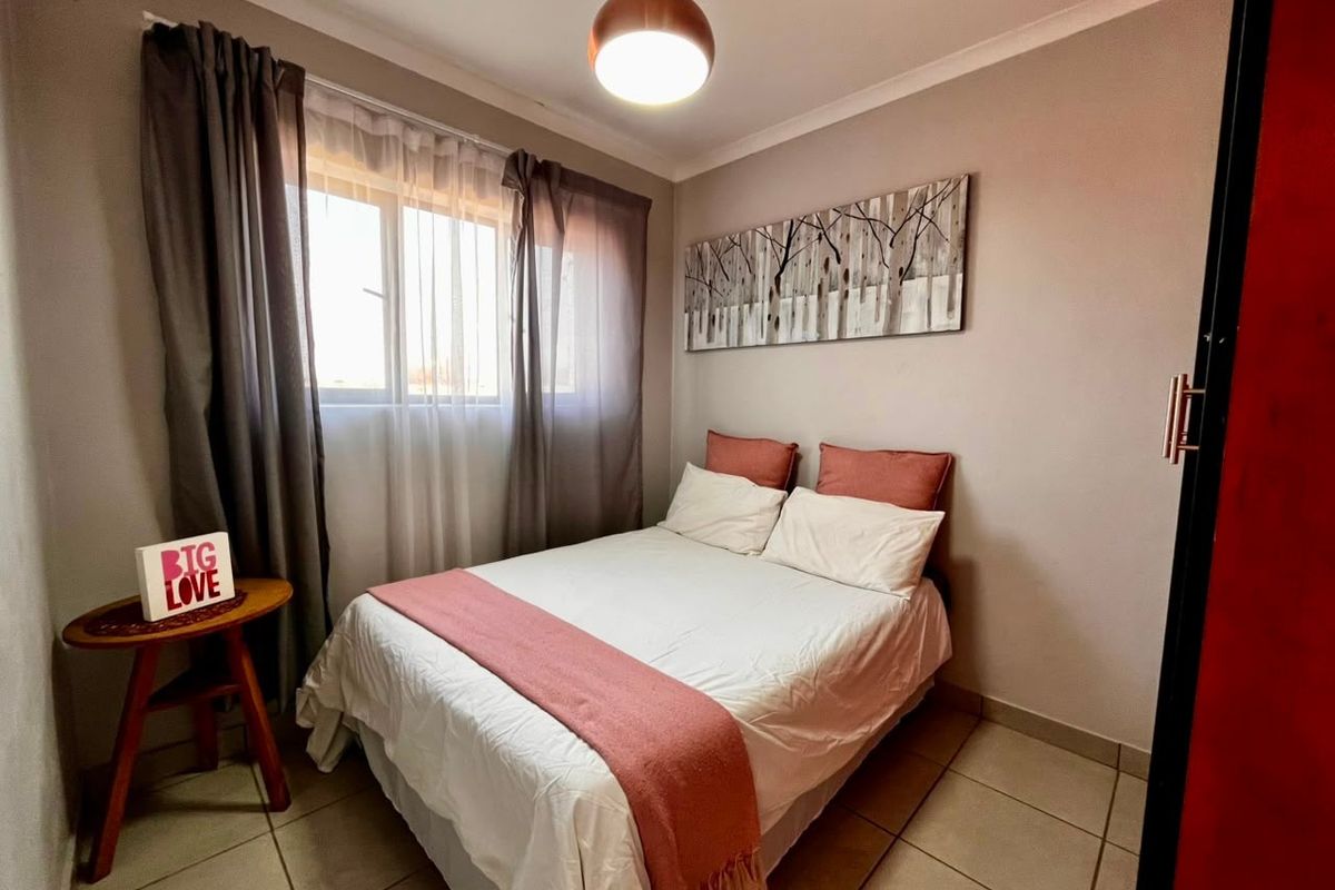 A cozy bedroom featuring neutral wall tones, tiled flooring, and a central pendant light fixture, providing a comfortable and functional sleeping space.