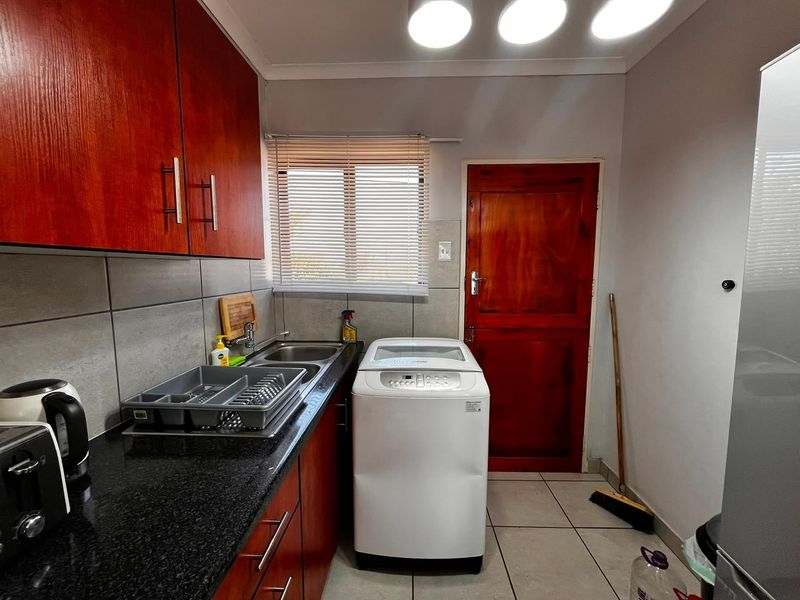 Functional laundry area featuring built-in cabinetry, granite countertops, a stainless steel sink, and tiled flooring with direct exterior access.