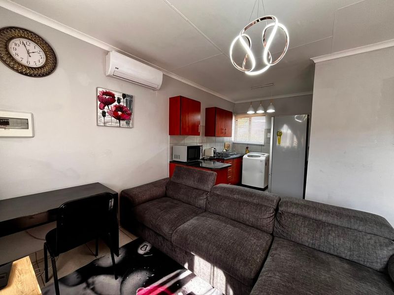 Open-plan living area featuring a compact kitchen with red cabinetry, tiled flooring, and a wall-mounted air conditioning unit.